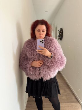 Kürklü kadın koridorda aynalı selfie çekiyor. Ev ortamında kendini ifade etme, moda ve günlük yaşam