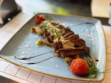 Restoran ortamında seramik tabakta soslu biftek ve sebze. Modern mutfak, aroma ve zarif yemek sunumu.