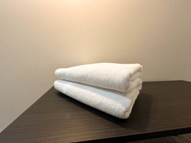 İç kısımda katlanmış beyaz havlular koyu ahşap masa üzerinde. Temizliği, konukseverliği ve spa ya da otel hizmetleriyle ilişkili rahatlığı yansıtır..