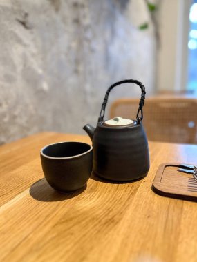 Sıcak kafenin iç tarafındaki ahşap masada fincanlı siyah seramik çaydanlık. Sakin, ritüel ve dikkatli çay içme deneyimi..