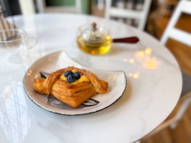 Beyaz mermer masada çay ile servis edilen yaban mersinli pasta. Rahat, sakin ve tatlı günlük ritüelleri, rahat bir kafe ortamında temsil eder..