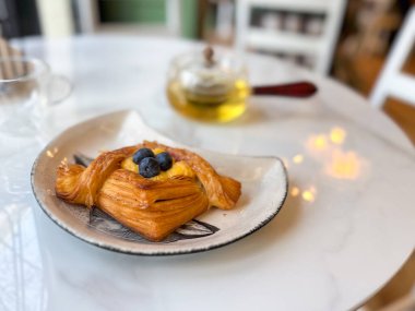 Beyaz mermer masada çay ile servis edilen yaban mersinli pasta. Rahat, sakin ve tatlı günlük ritüelleri, rahat bir kafe ortamında temsil eder..
