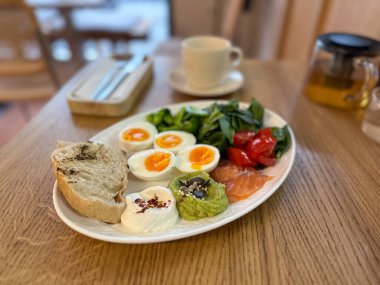 Tahta masada yumurta, somon ve sebzelerle dengeli kahvaltı. Sağlıklı beslenme, dikkatli rutin ve sabah enerji takviyesi.