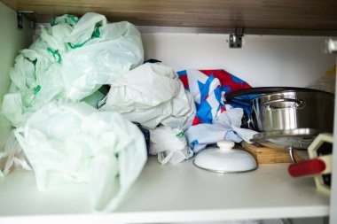 Naylon torbalar, tencereler ve dağınık malzemelerle dolu dağınık mutfak dolabı. Evdeki dağınıklık ve depolama sistemi eksikliği.