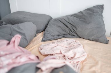 Kırışık yastıklar ve dağınık giysilerle yapılmamış yatak. Evdeki karmaşa ve günlük hayatta dağınık bir yaşam alanı.