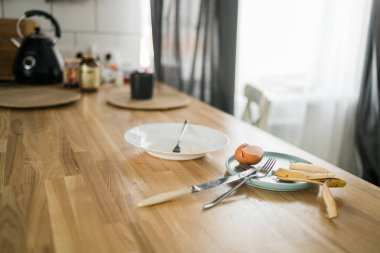 Dağınık bir mutfaktaki ahşap tezgahta kalan kahvaltı. Ev düzensizliği ve günlük ev işlerinde ihmal izleri..