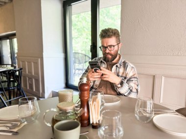 Kafe masasında telefonla konuşan bir adam. Modern yaşam tarzı, dijital alışkanlıklar ve sıradan şehir yemekleri..