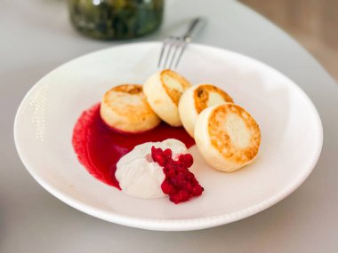 Syrniki ekşi krema ve böğürtlen sosuyla servis edilir. Geleneksel kahvaltı, köy konforu ve Doğu Avrupa mutfağı.