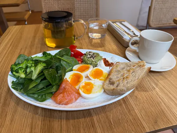 Sebzeli, yumurtalı ve somonlu sağlıklı kahvaltı tabağı, bitki çayıyla servis ediliyor. Modern bir kafede dengeli beslenme ve temiz yemek..
