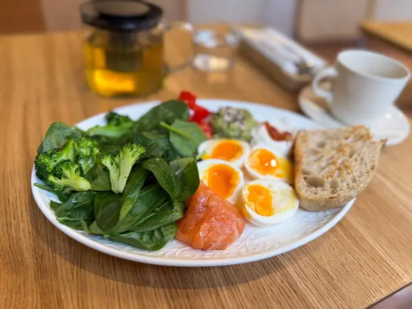 Sebzeli, yumurtalı ve somonlu sağlıklı kahvaltı tabağı, bitki çayıyla servis ediliyor. Modern bir kafede dengeli beslenme ve temiz yemek..