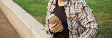 Adam açık havada kağıdın içinde sokak yemeği tutuyor. Fast food kavramı, günlük yaşam tarzı ve şehir parkında atıştırma..