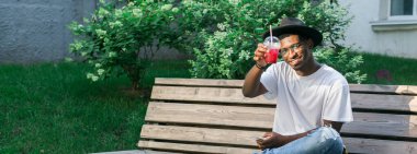 Afro-Amerikalı bir adam açık havada ferahlatıcı bir içkinin tadını çıkarıyor. Rahatlama, rahatlama ve yaz tatili konseptleri. Kopyalama alanı olan pankart.