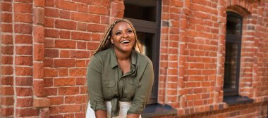 Afrika kökenli Amerikalı bir kadın güneşli bir günde şehir caddesinde dikilirken neşeyle gülüyor. Kentsel bir çevrede özgürlük, pozitiflik ve mutluluk.