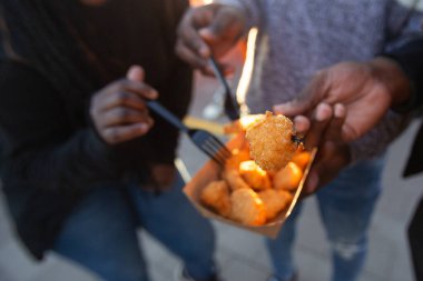 Afro-Amerikan arkadaşlarının yakın çekimleri, çatal kullanarak paket servis kutusundan atıştırmalıkları paylaşıyorlar. Yemek ve ellere odaklan, açık havada gündelik yemek ye.