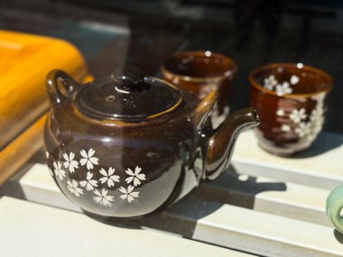 Çiçek desenli koyu kahverengi çaydanlık. Pencere ekranında beyaz kiraz çiçekleriyle süslenmiş seramik teaware seti