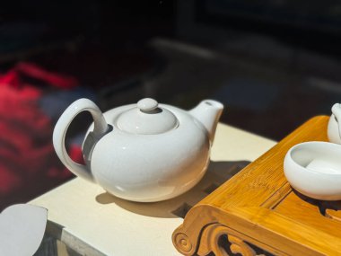 Işık yüzeyinde beyaz seramik çaydanlık. Kavisli saplı yuvarlak çaydanlık ve bambu çay tepsisinin yanında kısa hortum.