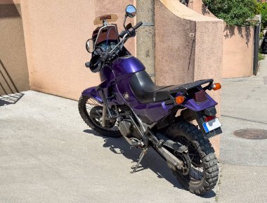 Mor motosiklet sıva duvarının yanına park edilmiş. Güneşli şehir caddesinde off-road lastikleri olan çift spor motosiklet.