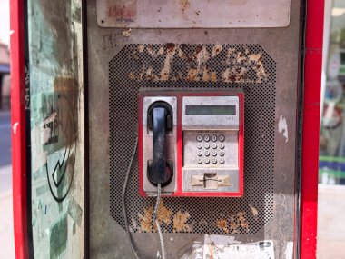 Old public payphone with keypad and receiver. Worn telephone booth with scratched metal panel and faded stickers.