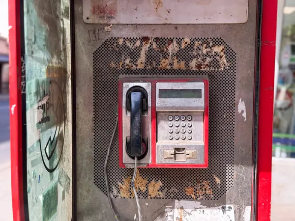 Tuş takımı ve alıcısı olan eski bir ankesörlü telefon. Üzerinde çizik metal paneller ve silinmiş çıkartmalar olan eski bir telefon kulübesi..