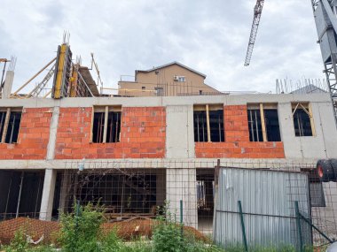 Kırmızı tuğlaları ve beton iskeleti olan kısmen inşa edilmiş bir bina. Yapısal elementleri ve devam eden çalışmaları gösteren kentsel gelişim sahnesi.