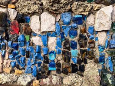Beton duvara gömülü renkli taş ve cam mozaik. Görüntü zanaatkarlığı ve dokunsal şehir detaylarını inceliyor..