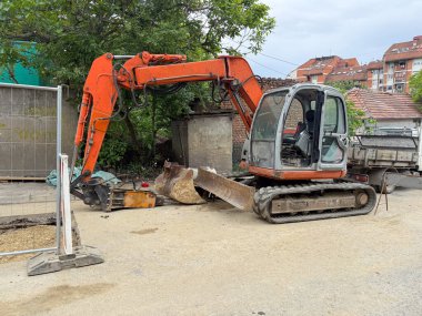 Turuncu kazıcı inşaat alanının yakınına park edilmiş. Bakım ekipmanları boşta kaldı