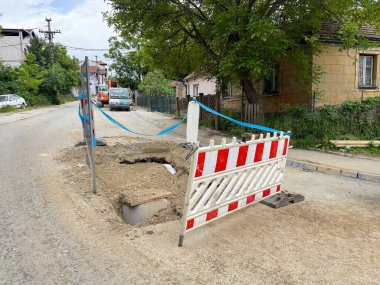 Sakin bir banliyö sokağında çitlerle çevrili açık bir kamu siperi. Yeraltı çalışmaları sırasında güvenlik bariyerleri sağlanır