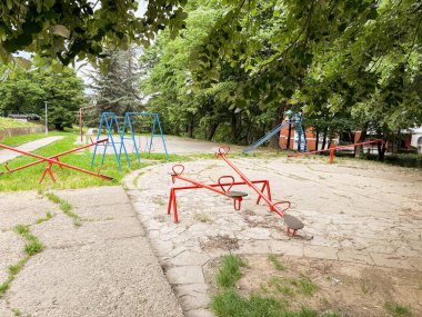 Tahterevalliler, salıncaklar ve yeşil ağaçların altında bir kaydırak olan boş bir eski oyun alanı. Şehirde sessiz ve nostaljik bir kamu alanı