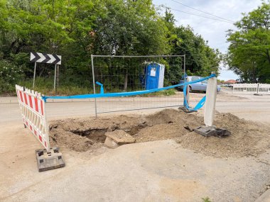 Yol inşaatında çit ve geçici bariyerlerle kazılmış bir delik. Yeraltı altyapı onarımının ilk aşaması