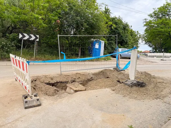 Yol inşaatında çit ve geçici bariyerlerle kazılmış bir delik. Yeraltı altyapı onarımının ilk aşaması
