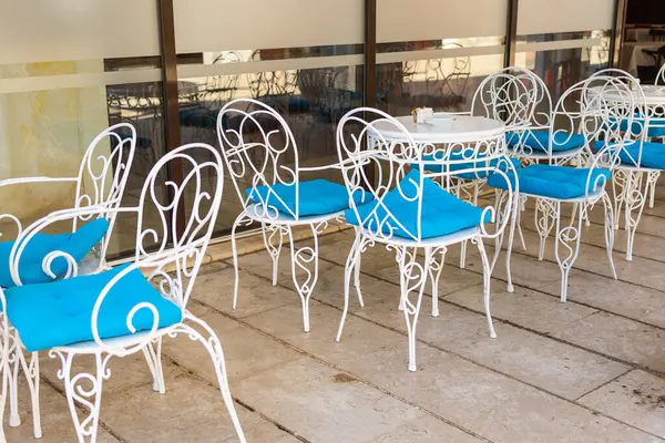 Cam duvarın yanında iki sandalye ve masa. Açık havada oturma, yaz misafirperverliği ve sessiz avluda Akdeniz kafe tasarımı.