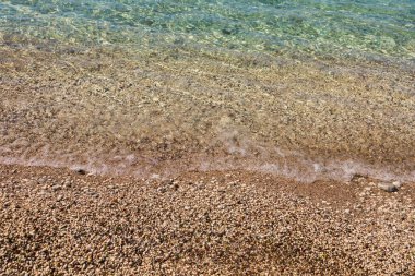 Çakıl taşı sahilinde temiz su. Kıyı dokusu, yaz sükuneti ve Akdeniz sahil çevrecilerinin doğal detayları.