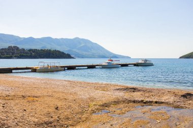Tekneleri ve dağ arkaplanı olan bir rıhtım. Karadağ 'ın Budva kentinde kıyı sükuneti, su taşımacılığı ve manzaralı yaz manzarası