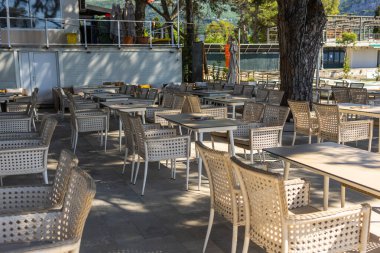 Ağaçların altındaki kafede boş hasır sandalyeler. Konukseverlik hizmeti, mevsimlik turizm ve kamusal alanlarda yaz tatili