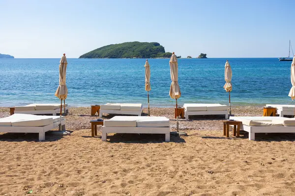 Adriyatik kıyısında boş güneş pansiyonları ve kapalı şemsiyeler. Karadağ 'ın Budva kentinde yaz plajı altyapısı ve kıyı turizmi.