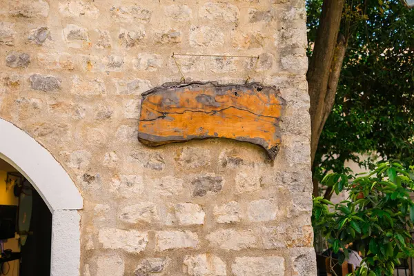 Binanın dışındaki taştan duvarda asılı boş ahşap tabela. Özel metin için klasik doku, el yapımı estetik ve boşluk