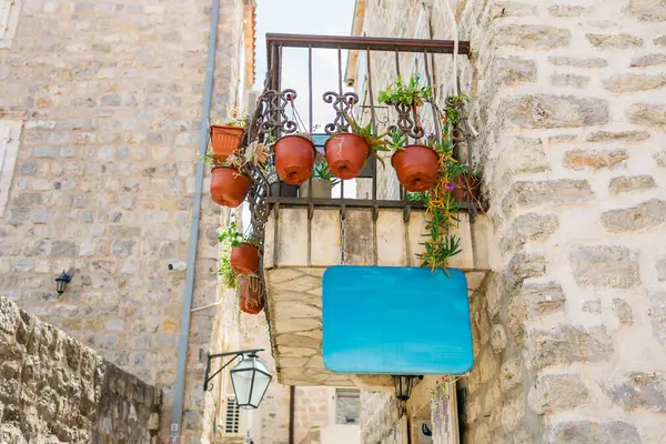 Çiçek saksıları olan küçük bir balkon ve taş bina fotokopi alanındaki boş mavi tabela. Akdeniz cazibesi, açık hava dekorasyonu ve klasik mimari