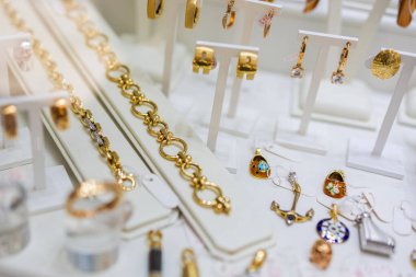 Altın bilezikler, küpeler ve takı mağazasında sergilenen tılsımlar. Lüks moda, aksesuar detay ve zarif perakende koleksiyonu.