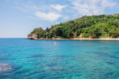 Turkuaz deniz ve orman kaplı kıyı şeridi olan tropik körfez. Doğa kaçışı, huzurlu plaj ve yaz tatili istirahatı. Karadağ ve Budva.