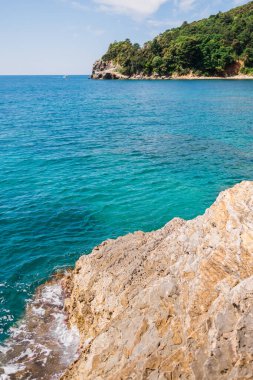 Rocky kıyı şeridi canlı turkuaz denizle buluşuyor. Kıyı manzarası, yaz doğası ve sakin açık hava keşfi.