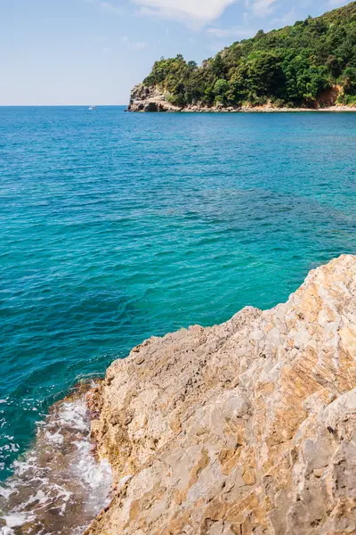 Rocky kıyı şeridi canlı turkuaz denizle buluşuyor. Kıyı manzarası, yaz doğası ve sakin açık hava keşfi.