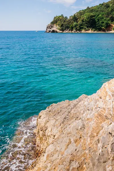 Rocky kıyı şeridi canlı turkuaz denizle buluşuyor. Kıyı manzarası, yaz doğası ve sakin açık hava keşfi.