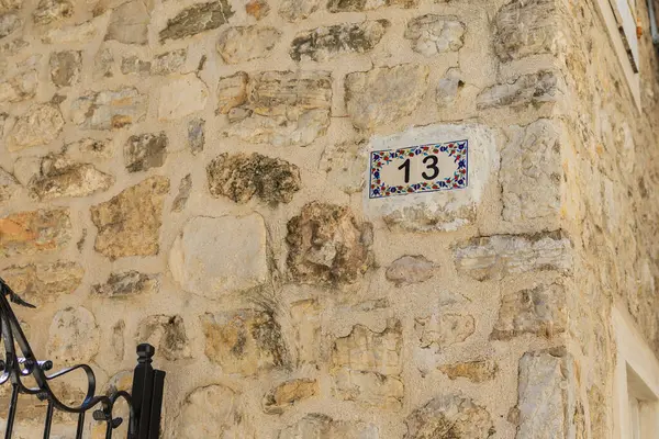 Taş duvar cephesinde 13 numaralı ev. Akdeniz tarzı, dekoratif fayans, kentsel ayrıntı ve sokak numaralandırması.