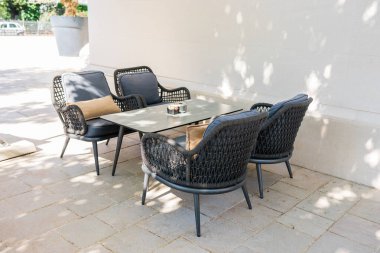 Örülmüş sandalyeli ve güneşli terasta masası olan açık hava oturma alanı. Modern veranda tasarımı, rahatlama bölgesi ve çağdaş açık hava yaşam tarzı konsepti