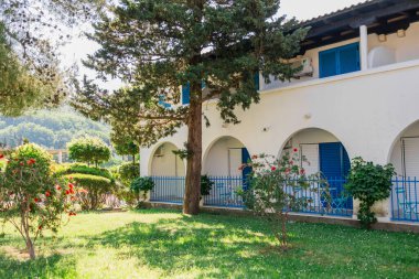 Önünde mavi panjurlar ve bahçe olan Akdeniz tarzı bir bina. Sakin bir tatil ortamı, otelin peyzaj tasarımı ve huzurlu bir açık hava.