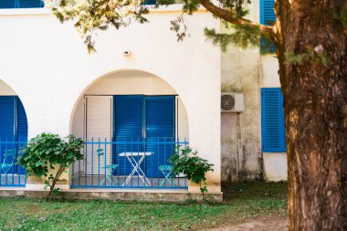Mavi panjurları, kemerli duvarları ve bahçe manzarası olan rahat bir otel terası. Akdeniz mimarisi, barışçıl geri çekilme ve büyüleyici açık hava oturma alanı.