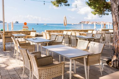 Deniz manzaralı açık bir kafe ve boş hasır sandalyeler. Akdeniz bölgesinde kıyı rahatlığı, yaz turizmi ve deniz kıyısında akşam yemeği..
