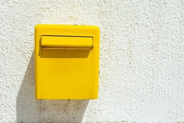 Parlak beyaz duvarda sarı posta kutusu. Posta servisi, iletişim sembolü ve güneşli bir ortamda sokak ayrıntıları. Boşluğu kopyala.
