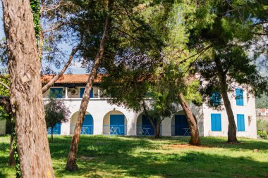 Çam ağaçlarının arkasındaki mavi panjurlu Akdeniz evi. Rahatlama, deniz kenarında yaşam ve yeşil ortamda Akdeniz cazibesi.