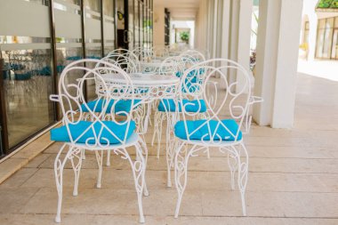 Güneşli verandada mavi yastıklı beyaz teras sandalyeleri. Açık hava zarafeti, Akdeniz eğlencesi ve yaz konukseverliği tasarımı.